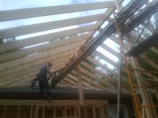 Rafters going up over a new addition with a worker on the wall in Peru