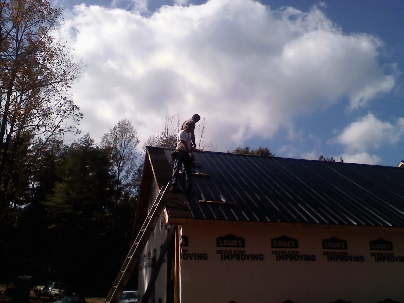 Roofer fastening dark metal panels high against a cloudy sky, from a Roof Inspection job in Peru
