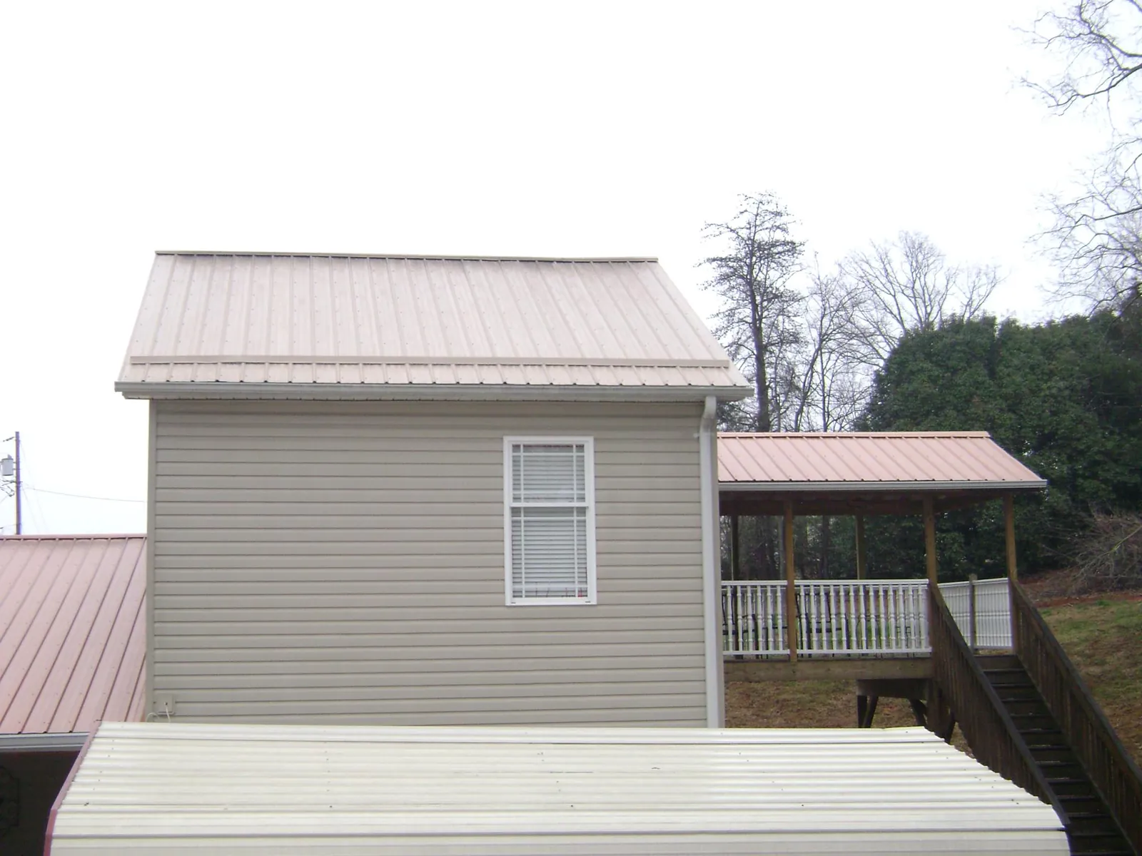 Tan metal roofs on a two story addition and attached porch, from a Roof Replacement job in Peru